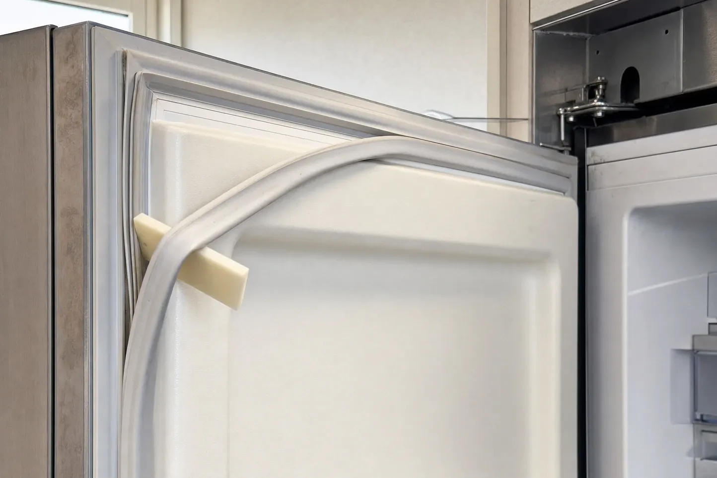 Close-up of a magnetic door gasket pulled clear of its channel at the top corner of a white door liner