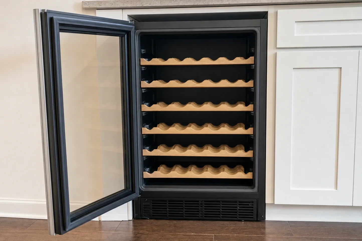 Empty undercounter wine cabinet with the glass door swung open, six scalloped wooden bottle racks and a vent grille below
